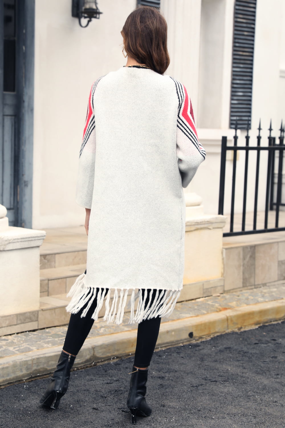 Back view of Women's Long white open cardigan with fringed hem, Black contrast trim, red and black  geometric print on shoulders